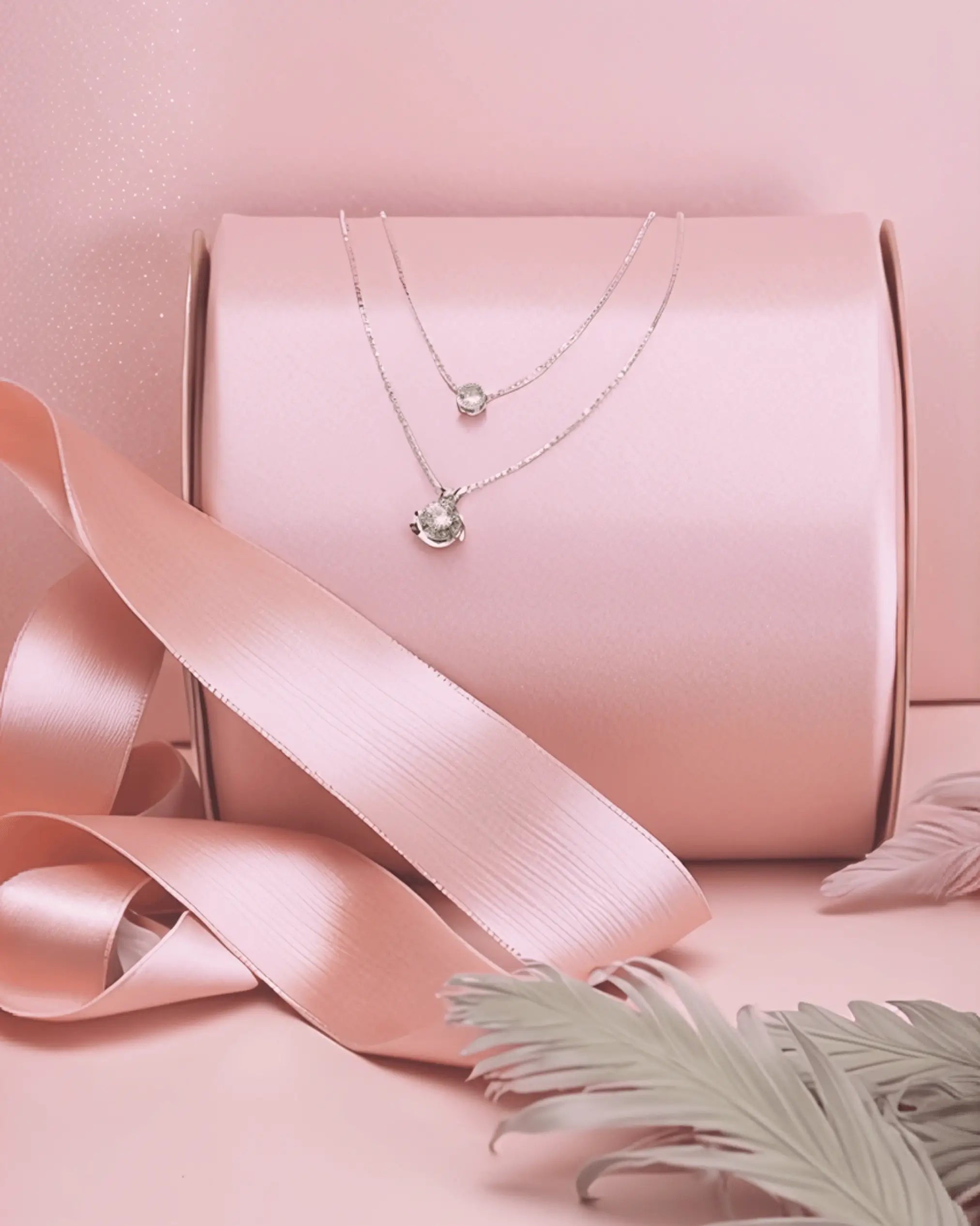 Delicate silver layered necklace featuring two separate chains with round solitaire cubic zirconia pendants, displayed on a pink gift box with a satin ribbon.
