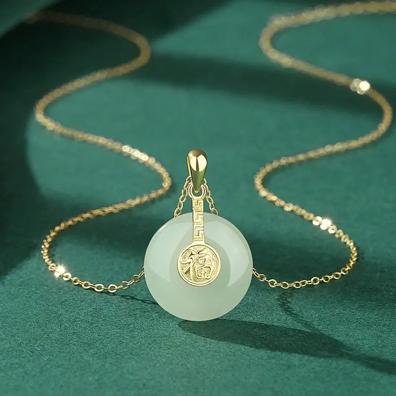 Close-up of a delicate gold chain necklace featuring a smooth, circular white jade pendant with a small gold medallion engraved with the Chinese Fu (福) character for luck.