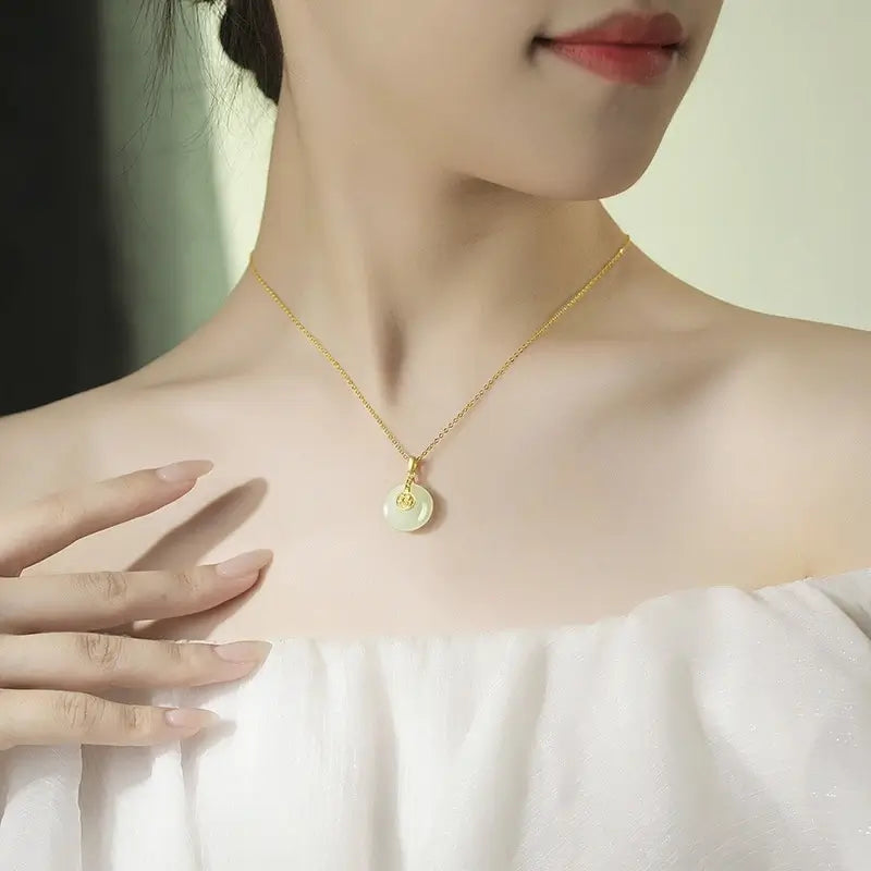 Woman wearing a delicate gold chain necklace with a small white jade circular pendant, demonstrating the piece at collarbone length.