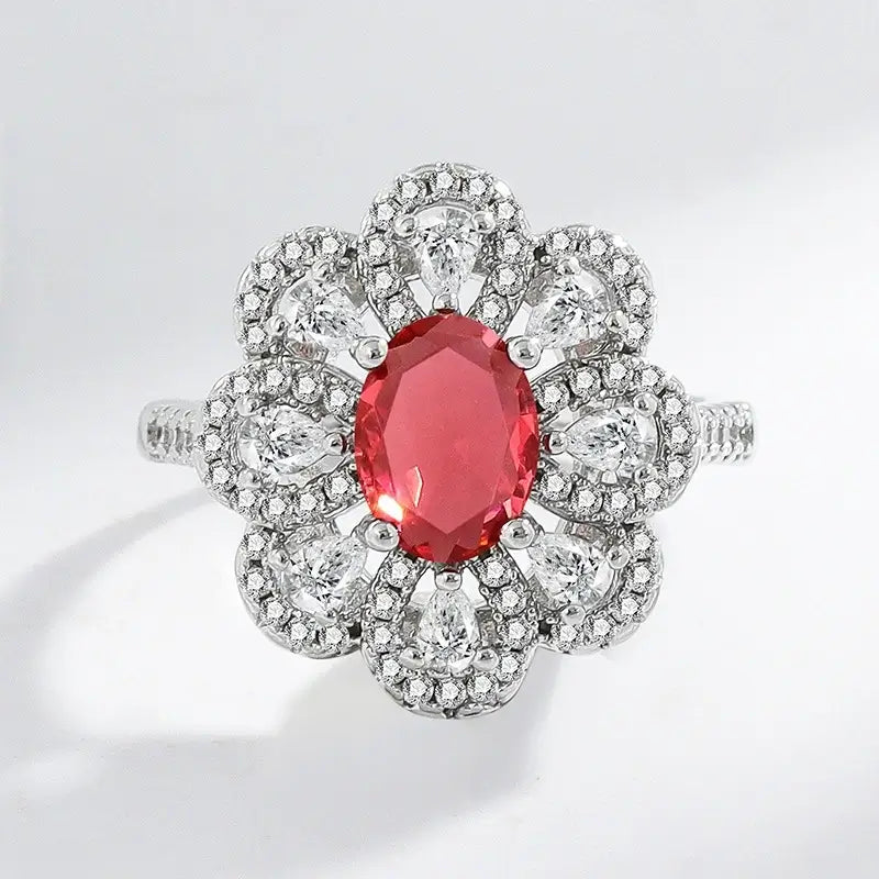Large cocktail ring with a flower cluster design in silver, featuring a central oval pink gemstone surrounded by a double halo of pear and pave-set cubic zirconia.