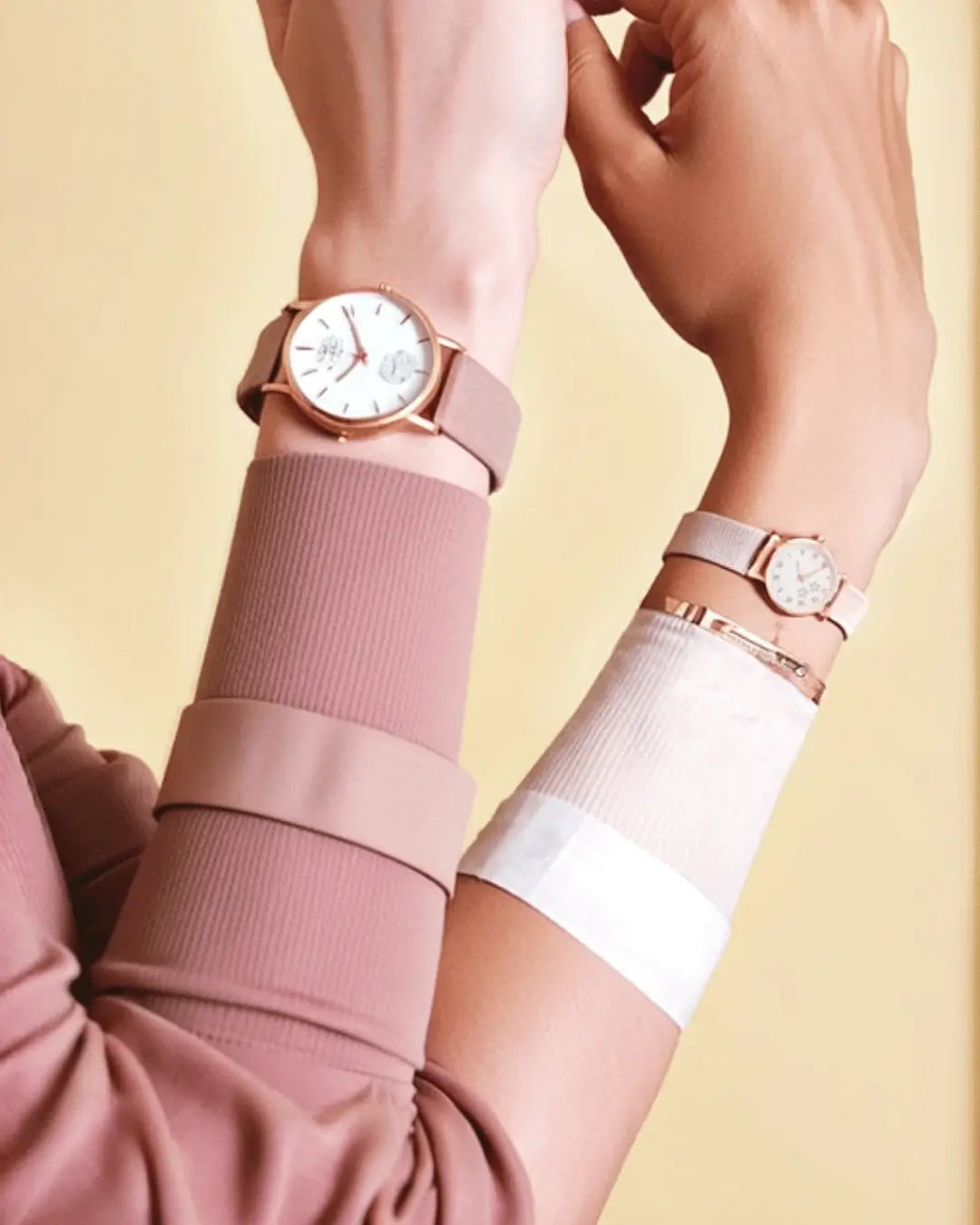 Two women's wrists showing contrasting sizes of rose gold watches with blush pink and taupe leather straps, stacked with slim gold bangles.