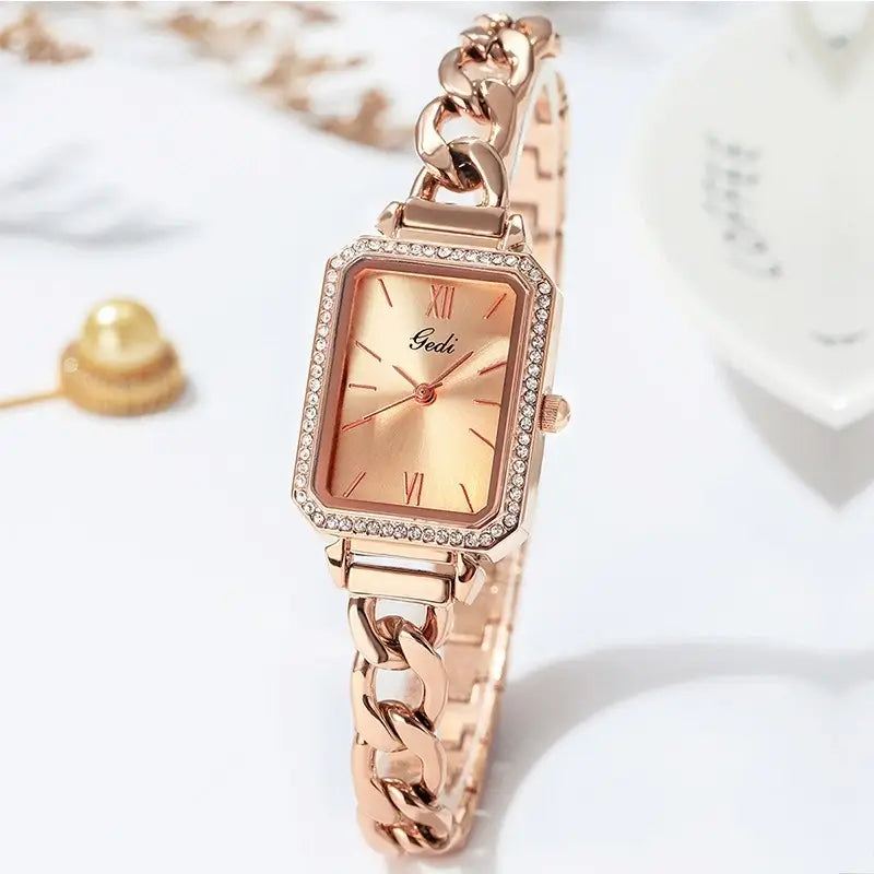 Rectangular rose gold watch featuring a thick chain bracelet, clear rhinestone bezel, and a metallic gold sunray dial.