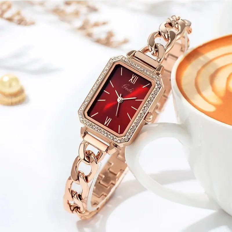 Luxury women's watch with a rose gold cuban link bracelet, rhinestone-studded rectangular case, and a vibrant ruby red dial.